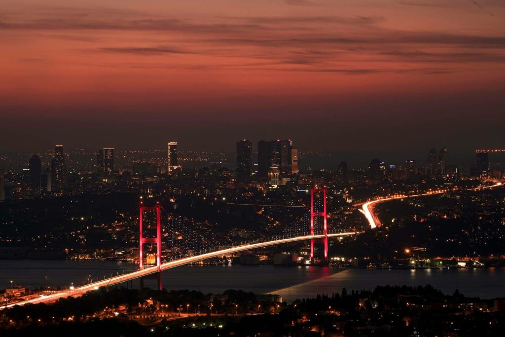 Stunning night view of the illuminated Bosphorus Bridge and Istanbul skyline under a red sky.