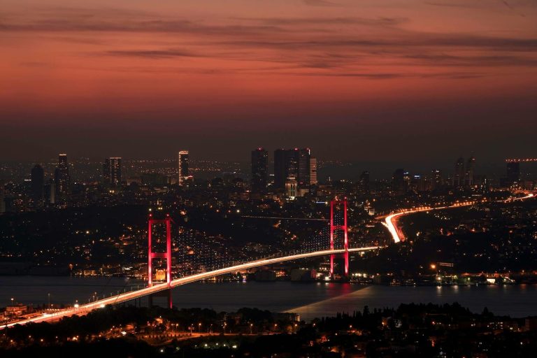 Stunning night view of the illuminated Bosphorus Bridge and Istanbul skyline under a red sky.