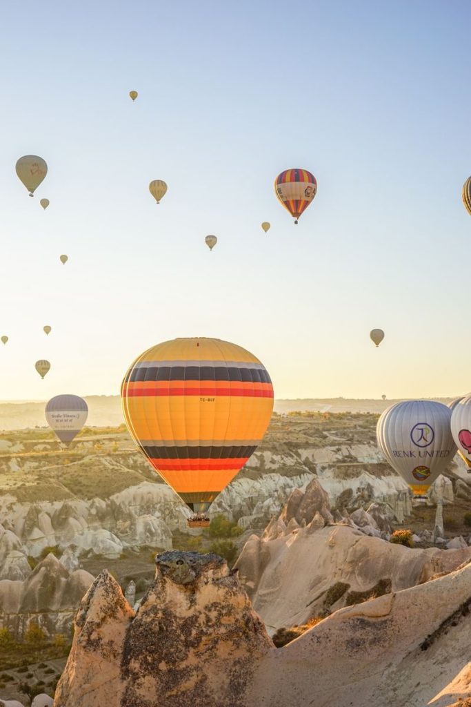 Vibrant hot air balloons soar over the unique rock formations of Cappadocia at sunrise.