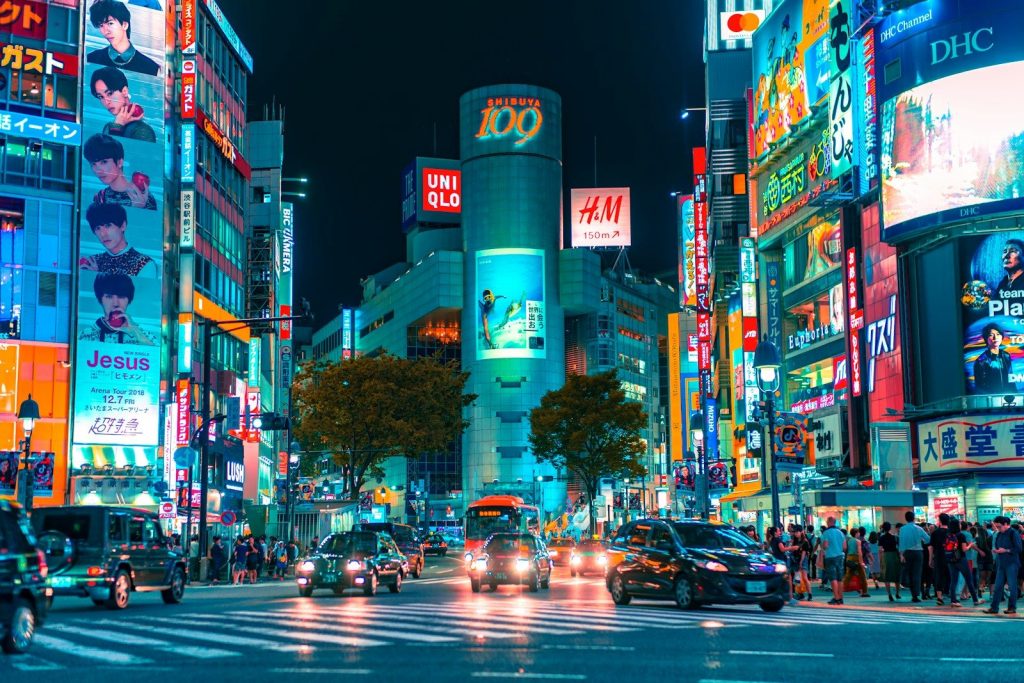 Cars driving through a neon-lit intersection in Shibuya, Tokyo, at night