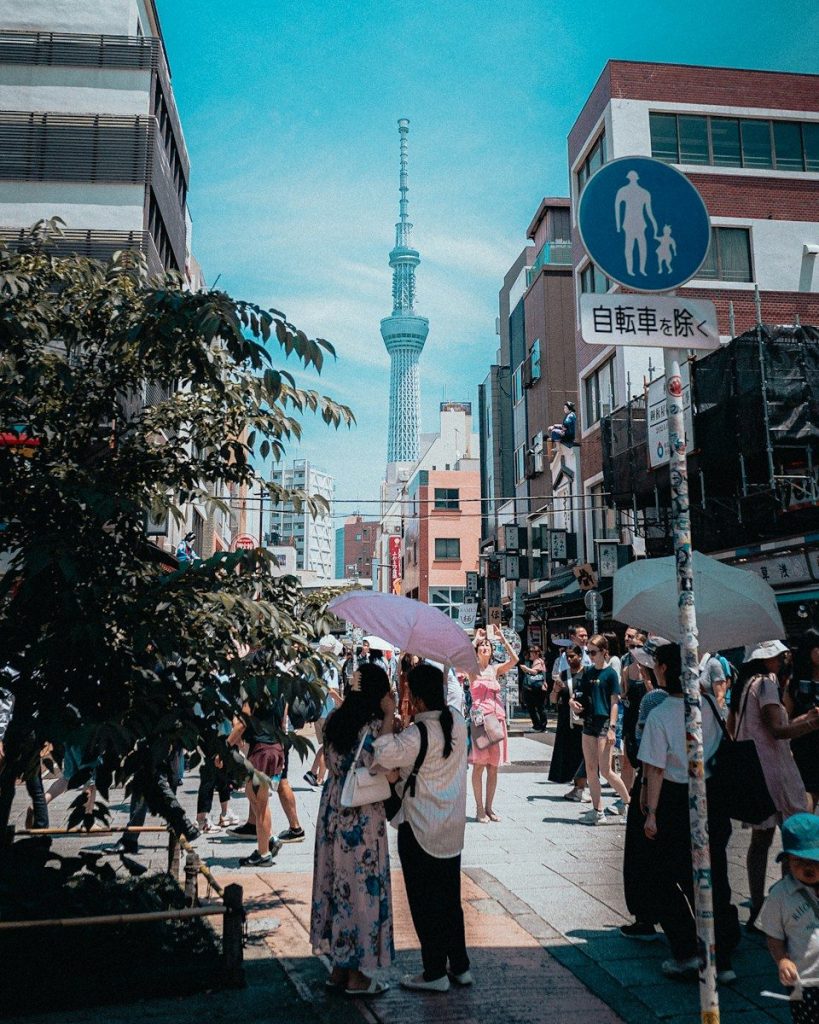 People with umbrellas on a street with a tall tower